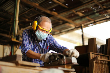 Senior Asian carpenter man is using hand planer with plank of wood in his own garage style workshop at retirement age for hobby