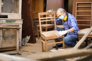 Senior Asian carpenter man is repairing wooden chair in his own garage style workshop at retirement...