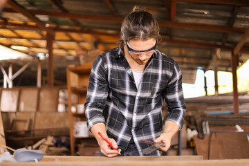 Caucasian carpenter man is using solid square measuring to scale the plank of wood in his own garage style workshop for hobby