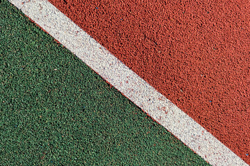 Abstract textured sport field background. Top view of green and red rubber turf surface with white...