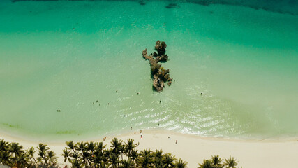White Beach of Boracay and people swim at turquoise azure sea near Grotto Willy's Rock upon which stands the Virgin Mary Statue. Copy space for text. Summer and travel vacation concept.
