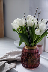 Beautiful bouquet of willow branches and tulips in vase on white table