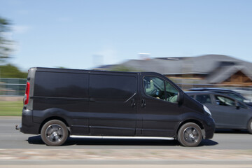 A black van is driving down the street at high speed. Motion blur