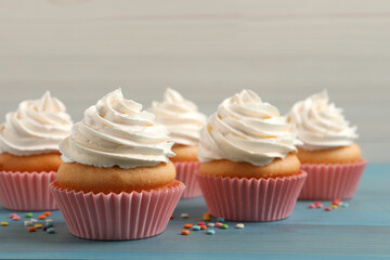 Delicious cupcakes decorated with cream on light blue wooden table