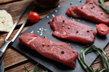 Fresh raw meat steaks and spices on wooden table, closeup