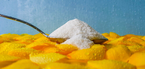 salt in a spoon is placed on a yellow flower and a sea color background