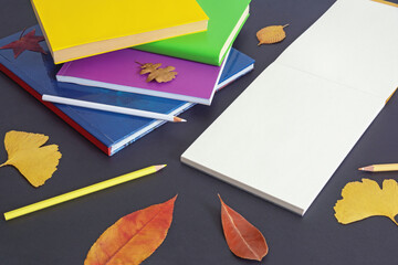 School concept. Stack of books, colorful colored pencils and open sketchbook on dark paper background. Autumn leaves. Free space for text or picture