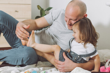 Father plays with little daughter 2-4 on floor. Dad tickles kids feet. Family having fun - obrazy, fototapety, plakaty