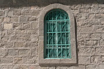 Fototapeta na wymiar Green window with wrought iron grating and stone wall