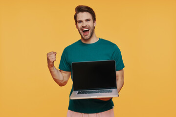 Handsome young smiling man in casual clothing carrying laptop and gesturing