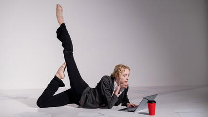 Barefoot ballerina dressed in a business suit poses for a laptop and drinks coffee. Flexible woman works at the computer
