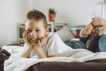 Father plays with his son 7-10 on bed. Dad tickles kids feet. Family, having fun