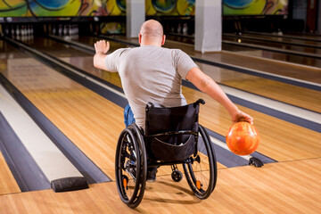 Young disabled man in wheelchair playing bowling in the club