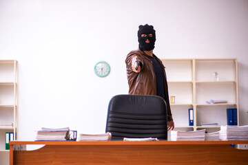 Young man in balaclava stealing information from the office