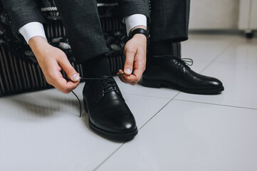 A man, a businessman, ties long shoelaces on leather black shoes, shiny with cream, with his hands...