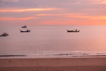 Obraz premium beautiful soft orange and pink sun light sunset in sea behind island. silhouette fisherman boat. calm and romantic place in thailand