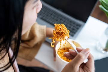 business woman eating spicy noodles at work place sitting at office with notebook on desk ,...