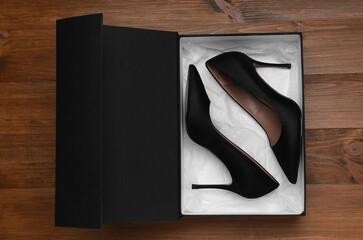 Pair of stylish shoes in black box on wooden background, top view