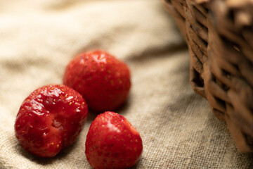 three strawberries lie on a burlap cloth and a basket side by side. Copy space