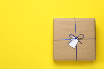 Parcel wrapped in kraft paper with tag on yellow background, top view. Space for text