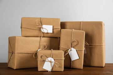 Parcels wrapped in kraft paper with tags on wooden table against light grey background