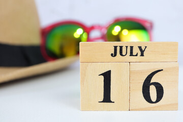 Cube wooden calendar showing date on 16 July. Wooden calendar with date and hat, sunglasses on the...