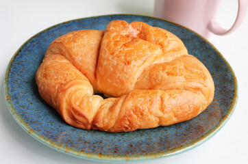 Delicious, fresh croissant on plate and pink coffee mug on the table.