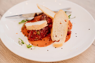tartare with sauce, microgreen and bread on a white plate.
