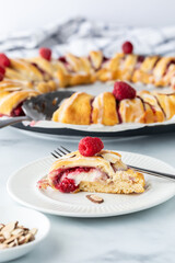 Close up view of a slice from a raspberry crescent ring with the full ring in behind.