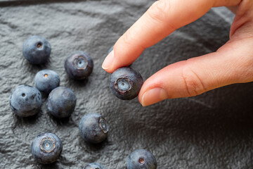 blueberry berry in the fingers of a woman's hand. Textured black background. Close-up, selective focus on the berry