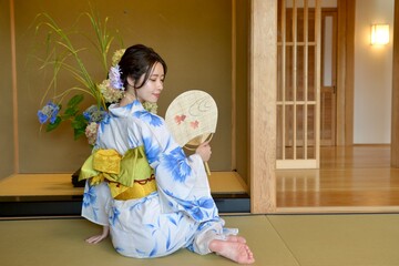 畳の上に座り団扇を手にたたずむ浴衣姿の美しい女性