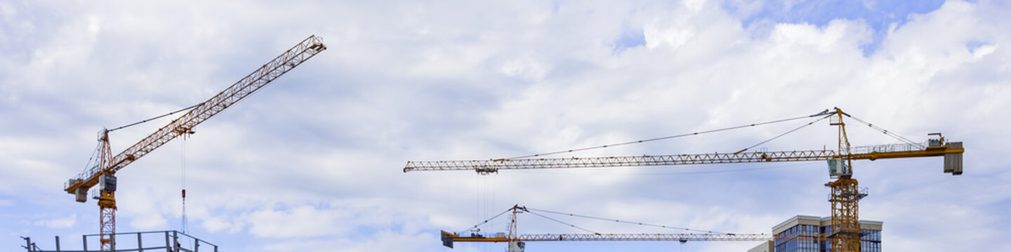 Construction cranes on the background of the sky with clouds. Panoramic image.