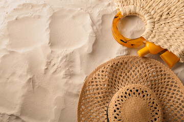 Straw hat and bag with sunscreen on sand, flat lay. Space for text