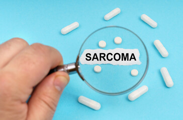 A man looks through a magnifying glass at pills and a leaf with the inscription - SARCOMA
