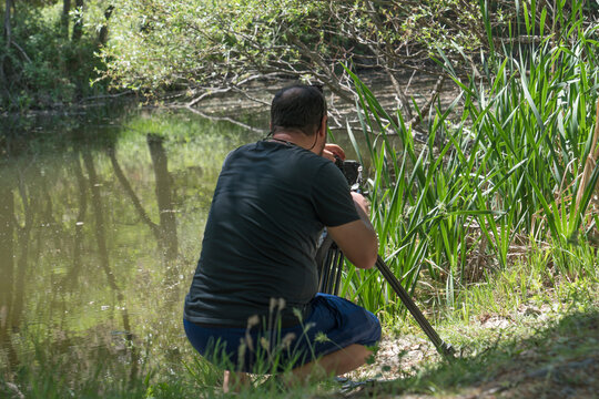 close up photographer with a tripod and camera makes photos at pond shore.Unfocused