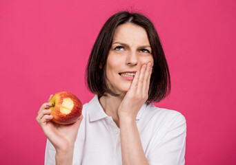 Beautiful young woman bites a big apple and has a toothache