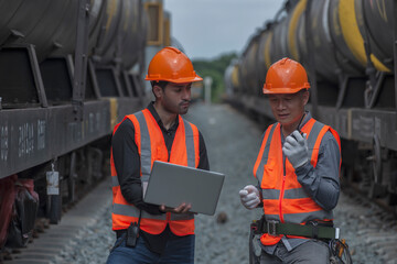workers at work. two engineer co-work on laptop between oil tank bogie in station. 