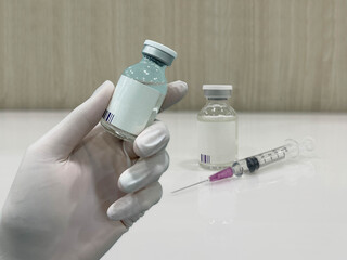 Hand in medical glove holding a medicine bottle,  medicine bottle, and syringe blur background.