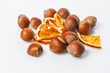 Ripe wild hazelnuts and pieces of dried orange. Stack of hazelnuts and orange chips on a white background. Filbert nuts. Natural organic product. Copy space. Close-up.