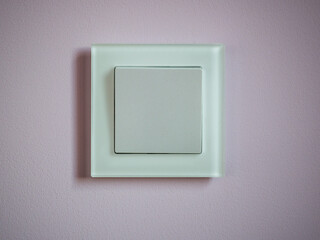 A one-button electric switch in a glass frame on a pink wall.