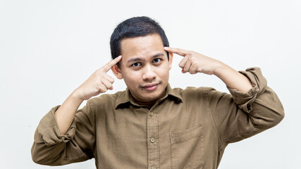 Obraz premium Young handsome Asian Malay man with wearing casual brown shirt and smiling pointing to head with both finger, great idea or thought, good memory on isolated white background. Positive thinking.