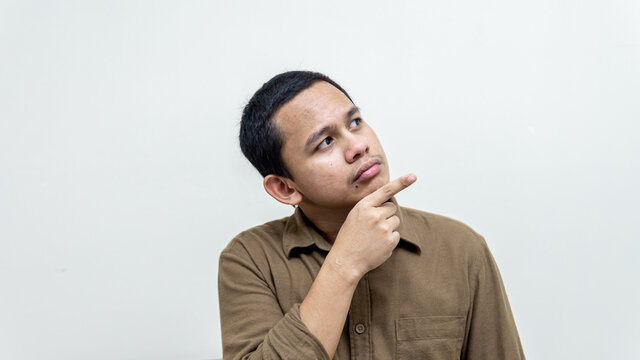 Serious face expression of young Asian Malay man wearing casual brown shirt with hand pointing on empty space with isolated white background.