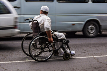 Fototapeta na wymiar A man in a wheelchair asks for alms from the drivers of the main city highway.