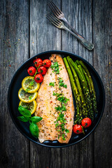 Roasted trout fillet with asparagus and vegetables served on black plate on wooden table
