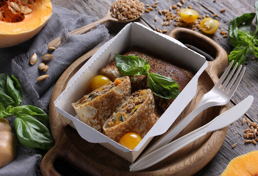 Food for delivery. Pancakes with pumpkin, meat, spelt and herbs in a box on a gray wooden table. Rustic. Background image, copy space