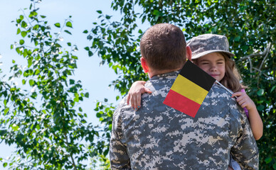 Reunion of soldier from Belgium with family, daughter hug father. A girl holds the flag of Belgium...
