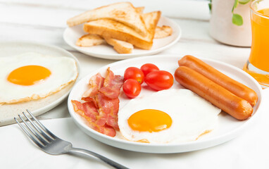 Breakfast with fried eggs, sausages,tomatoes,orange juice and bacon on white wood table.