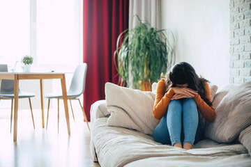 Sad woman in deep depression is sitting on the couch and crying and thinking about the bad thing