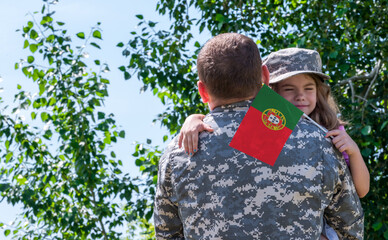 Reunion of soldier from Portugal with family, daughter hug father. A girl holds the flag of...