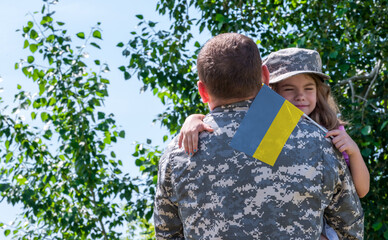 Reunion of soldier from Ukraine with family, daughter hug father. A girl holds the flag of Ukraine...